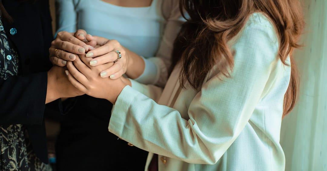 A group of women holding hands, offering each other comfort, community, and support. | The Unexpected Benefits of Community for Those With Chronic Illness